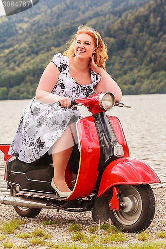 Image of Red-haired beauty with overweight on a red scooter
