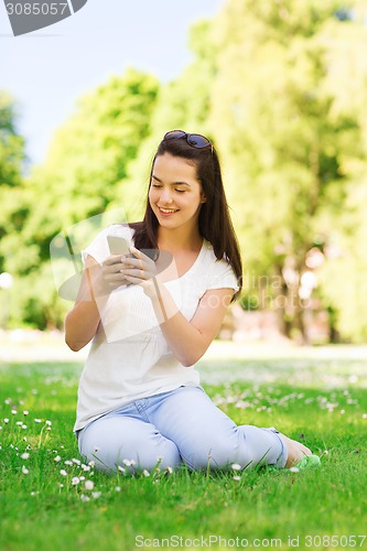 Image of smiling young girl with smartphone sitting in park