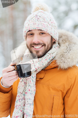 Image of smiling young man with cup in winter forest