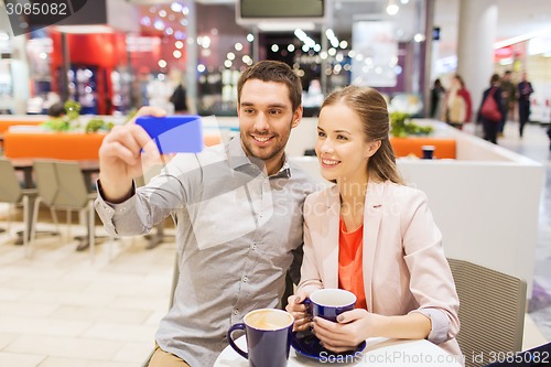 Image of happy couple with smartphone taking selfie in mall