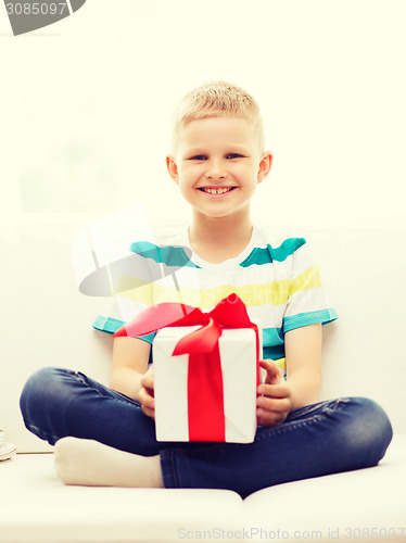 Image of smiling little holding gift box sitting on couch