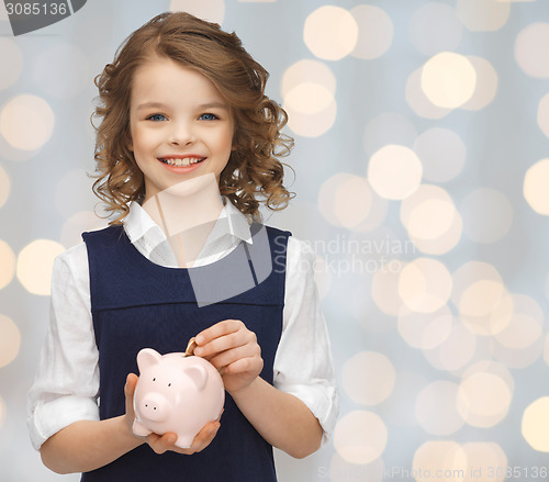 Image of smiling girl putting coin into piggy bank