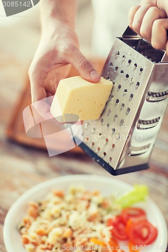 Image of close up of male hands grating cheese over pasta