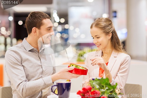 Image of happy couple with present and flowers in mall