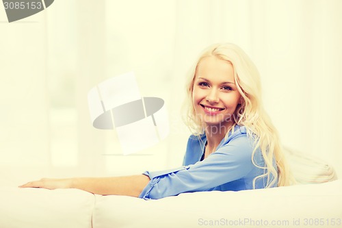 Image of smiling young woman lying on sofa at home