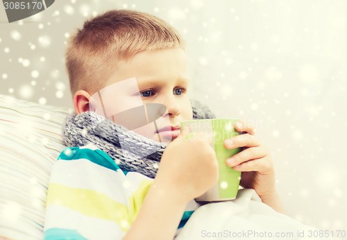 Image of ill boy with flu in bed drinking from cup at home