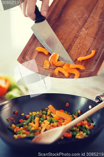 Image of close up of male hand adding peppers to wok