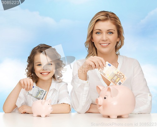 Image of mother and daughter putting money to piggy banks