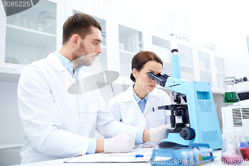 Image of scientists with clipboard and microscope in lab