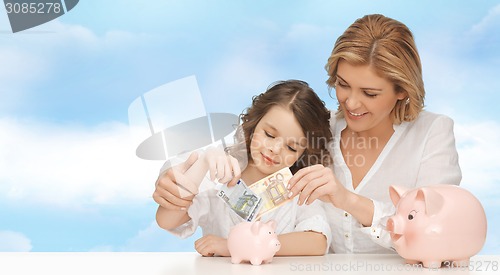 Image of mother and daughter putting money to piggy banks