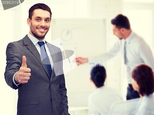 Image of handsome buisnessman showing thumbs up in office