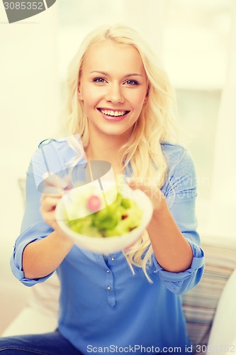 Image of smiling young woman with green salad at home