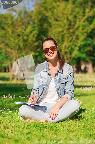 Image of smiling young girl with notebook writing in park