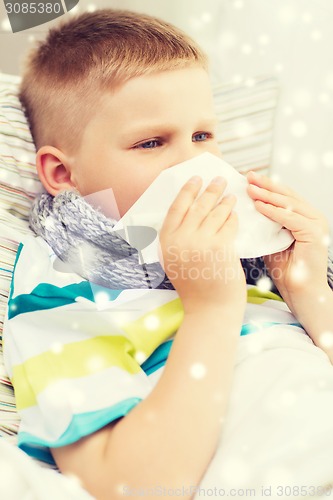 Image of ill boy blowing nose with tissue at home