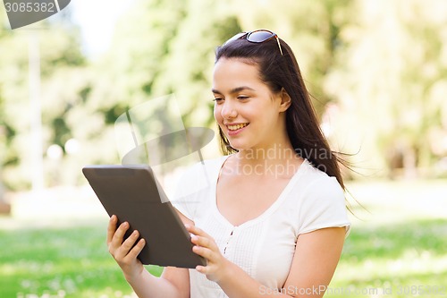 Image of smiling young girl with tablet pc sitting on grass