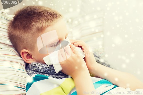 Image of ill boy blowing nose with tissue at home