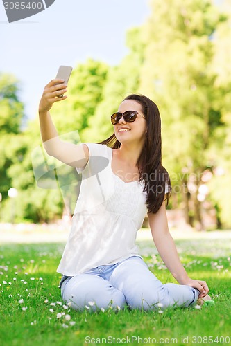 Image of smiling young girl with smartphone sitting in park
