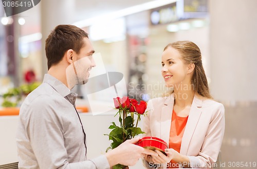 Image of happy couple with present and flowers in mall