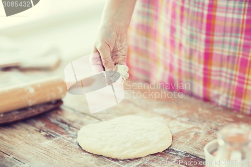 Image of closeup of female hand sprinkling dough with flour