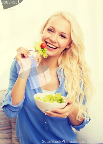 Image of smiling young woman with green salad at home