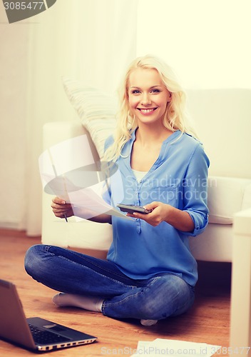 Image of smiling woman with papers, laptop and calculator