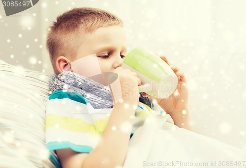 Image of ill boy with flu in bed drinking from cup at home