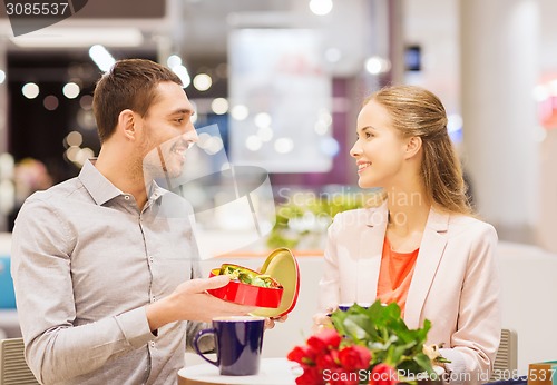 Image of happy couple with present and flowers in mall