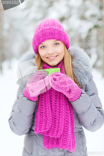 Image of smiling young woman with cup in winter forest