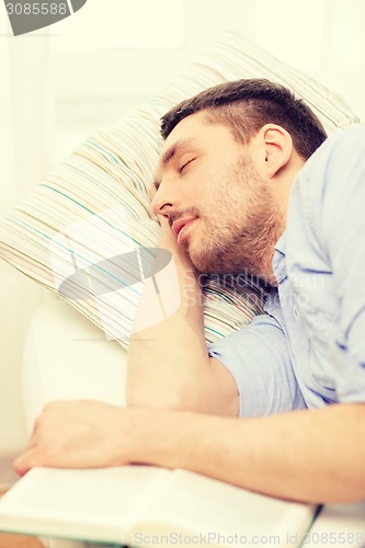 Image of calm young man lying on sofa at home with book