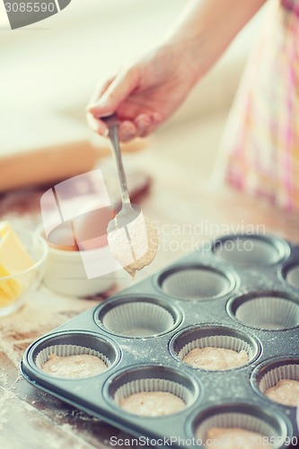 Image of close up of hand filling muffins molds with dough