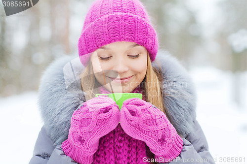Image of smiling young woman with cup in winter forest