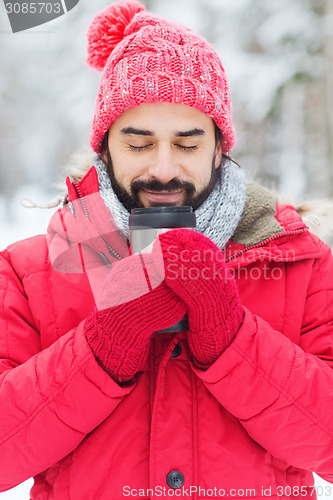 Image of smiling young man with cup in winter forest