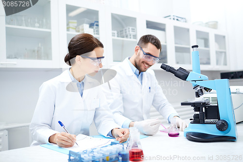 Image of scientists with clipboard and microscope in lab