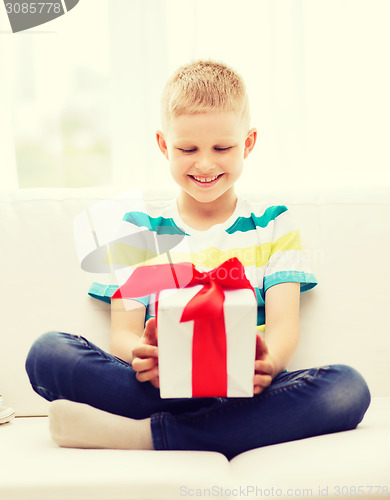 Image of smiling little holding gift box sitting on couch