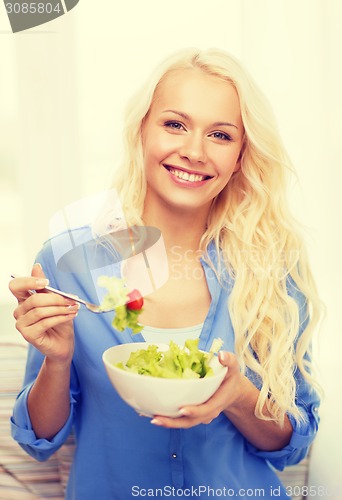 Image of smiling young woman with green salad at home