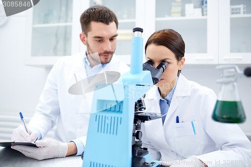 Image of scientists with clipboard and microscope in lab