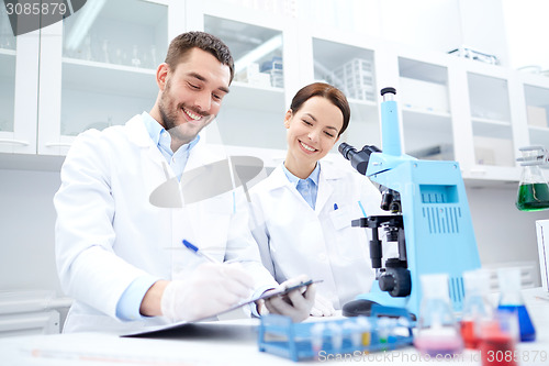 Image of scientists with clipboard and microscope in lab