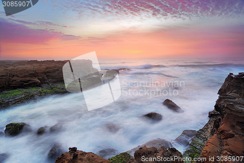 Image of Stunning sunrise and ocean flows over tidal rocks