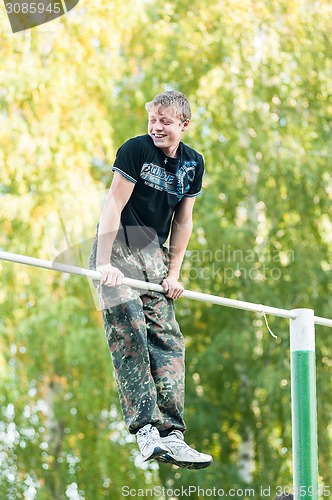 Image of Smiling boy shows own skill on horizontal bar