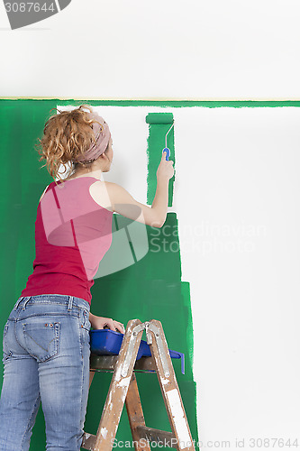 Image of Woman on ladder painting wall green