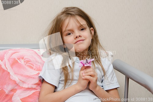 Image of Five year old girl sitting in bed with a flower