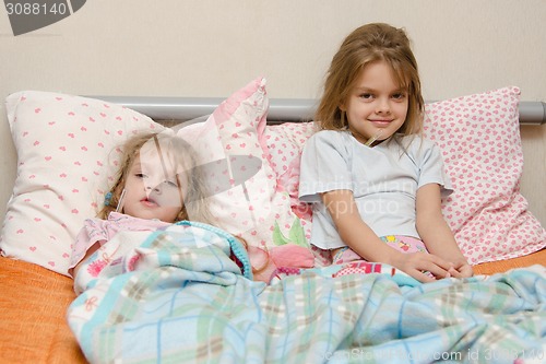 Image of Two girls sick in bed with a thermometer