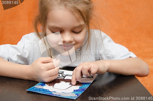 Image of The girl at the table playing sand applique
