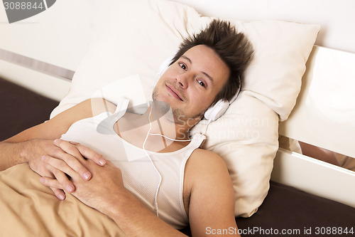 Image of Smart guy lies in bed and listens to music