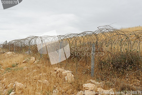 Image of Barbed tape or razor wire fence across the desert hill on cloudy day