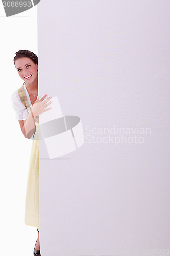 Image of Young woman in dirndl hiding behind a wall