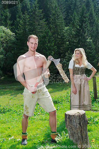 Image of Bavarian couple in love chopping wood in fashionable dress clothing