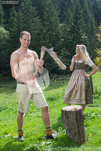 Image of Scene of a Bavarian couple in traditional costumes chopping wood