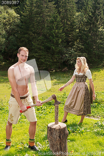 Image of Young Bavarian man with leather trousers chopping wood on a summer pasture