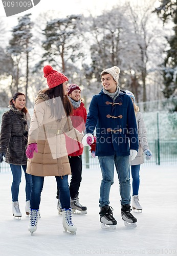 Image of happy friends ice skating on rink outdoors